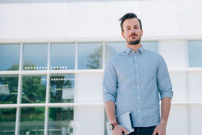 Young man looking away while standing against built structure