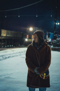 Woman standing on snow covered street at night