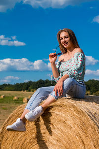 Portrait of young woman sitting on field against sky