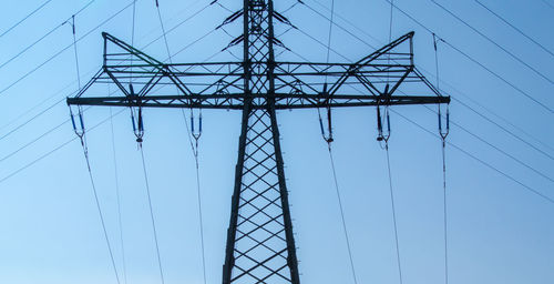 Low angle view of electricity pylon against clear blue sky