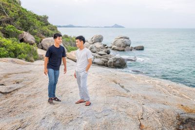 Friends standing on rock by sea against sky