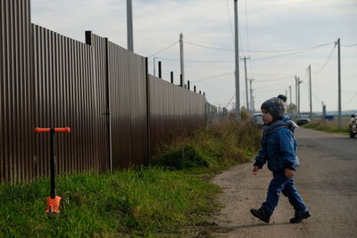 Side view of boy walking on road against sky