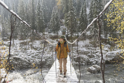 Hiker walking on bridge over river in winter forest