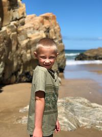 Portrait of boy standing at beach against sky