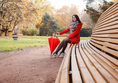 Woman sitting on bench against trees during autumn