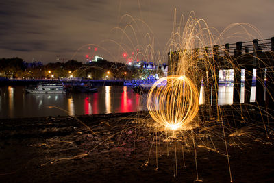 Light trails over river against sky at night