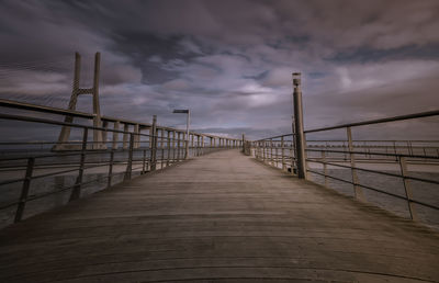 Footbridge over sea against cloudy sky