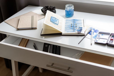 An open watercolor sketchbook lies on a white table.