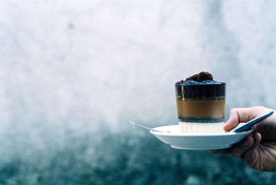 Cropped hand having drink in cup against wall