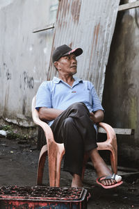 Full length of man looking away while sitting outdoors