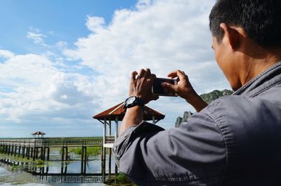 Rear view of man photographing gazebo against sky