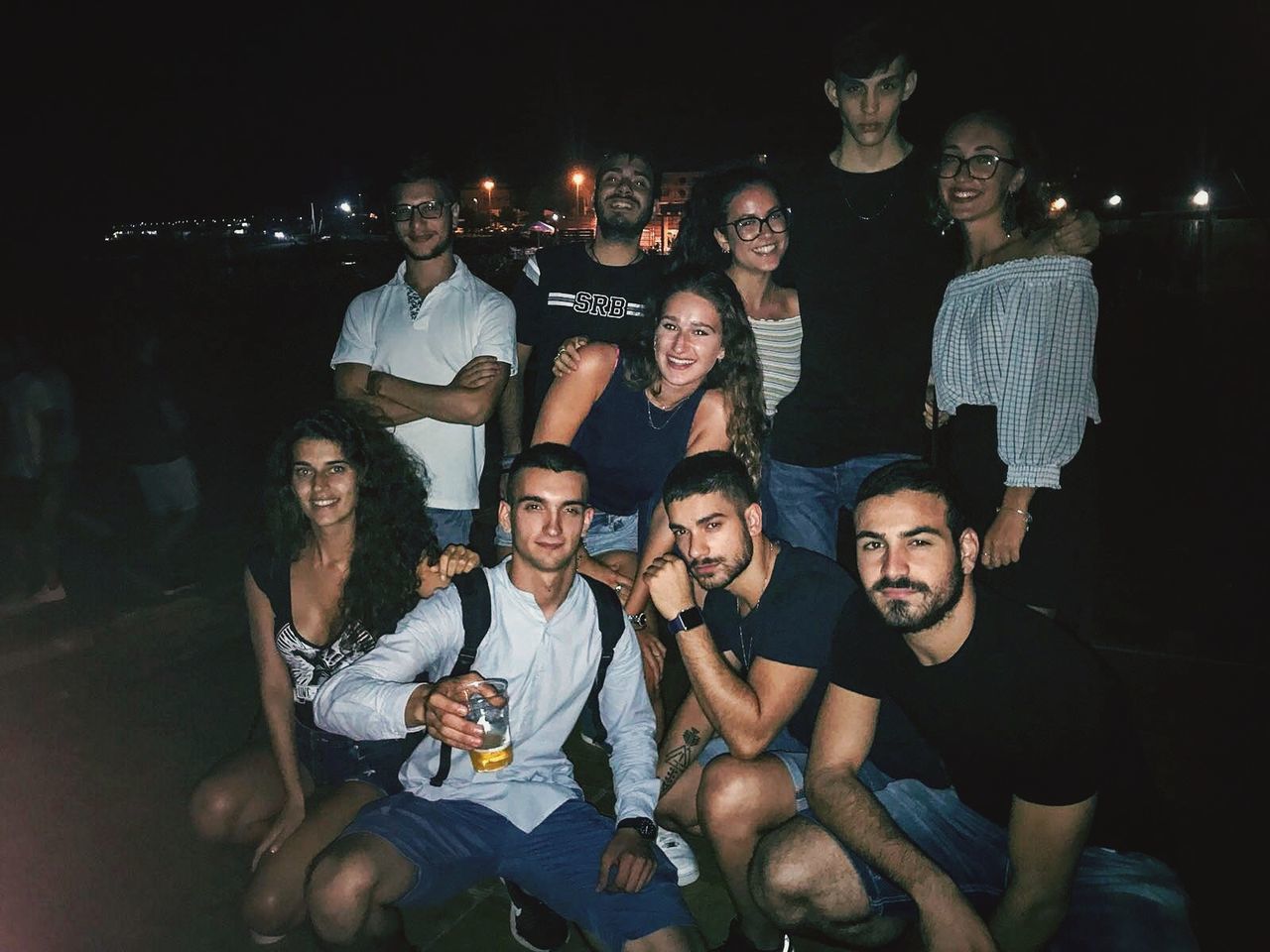 young adult, young men, group of people, young women, sitting, casual clothing, real people, night, leisure activity, togetherness, front view, lifestyles, smiling, men, people, happiness, friendship, illuminated, nightlife