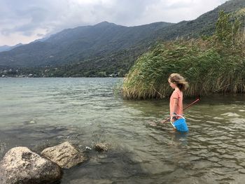 Full length of boy on rock by lake against sky