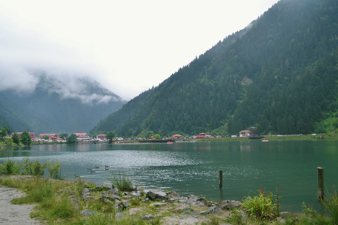 mountain, water, mountain range, tranquil scene, tranquility, scenics, lake, beauty in nature, sky, nature, tree, boat, idyllic, non-urban scene, day, landscape, outdoors, hill, calm, lakeshore, remote, no people, plant, growth, non urban scene, green color, grass, cloud - sky