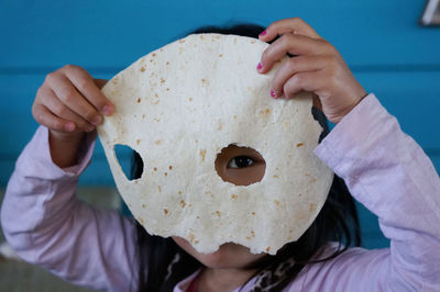 Close-up of girl holding flat bread with holes over face