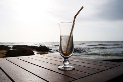 Wineglass on table by sea against sky