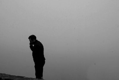 Side view of young man standing against clear sky