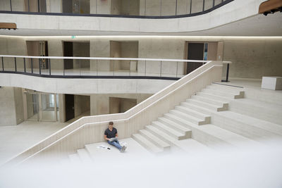 Young man sitting on stairs in office building using laptop