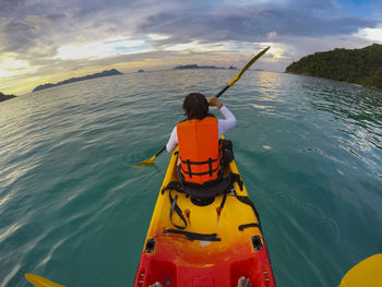 Rear view of woman kayaking in sea against sky