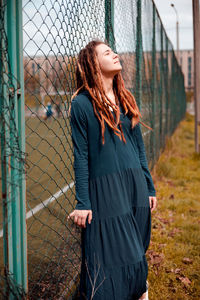 Young woman standing against chainlink fence