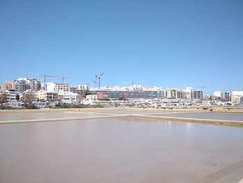 Buildings by sea against clear blue sky