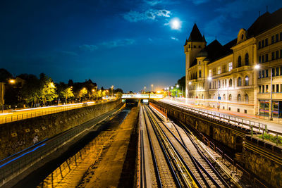 Railroad tracks in city against sky at night