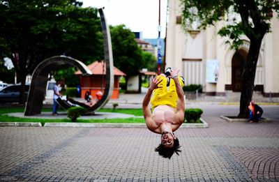 Shirtless man backflipping on footpath in city