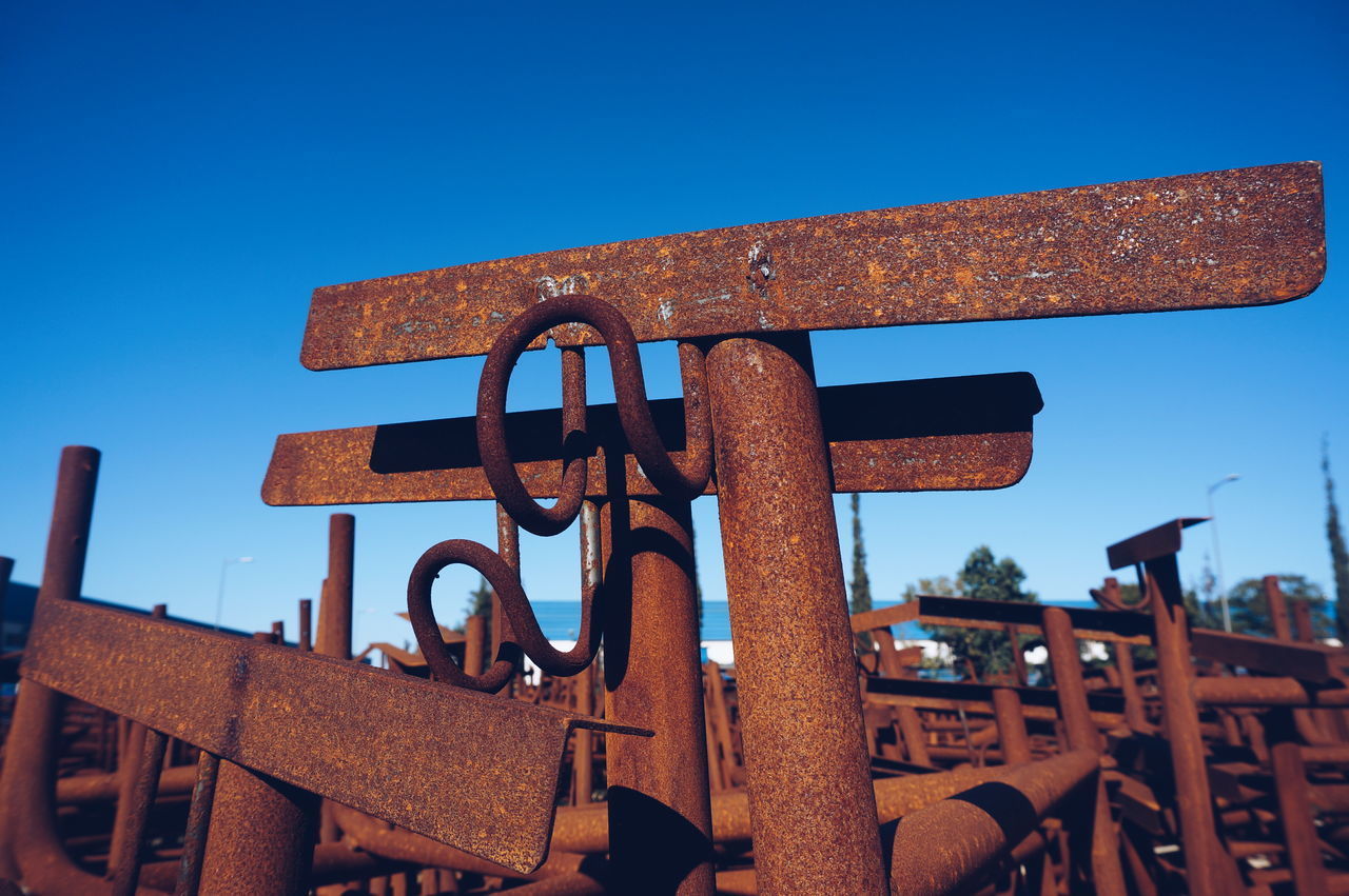 LOW ANGLE VIEW OF RUSTY MACHINE AGAINST BLUE SKY