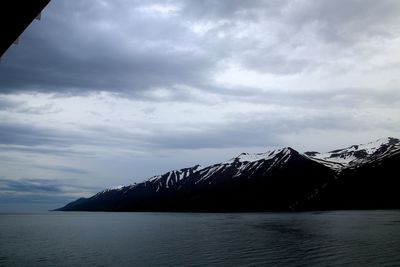 Scenic view of sea by snowcapped mountains against sky