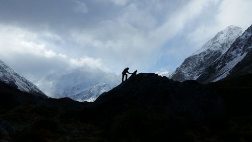 Hikers on mountain peak against cloudy sky