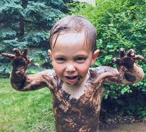 Portrait of shirtless boy covered with mud standing in yard