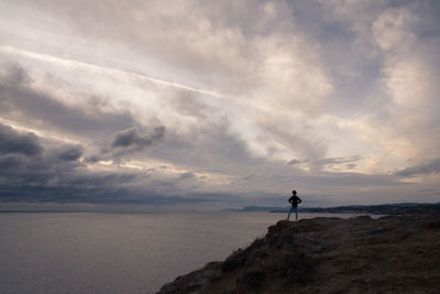 Man standing on rock by sea against sky