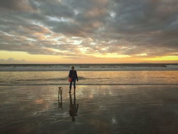 Woman standing on beach against sky during sunset