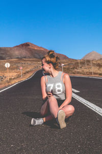 Young woman on road against clear blue sky