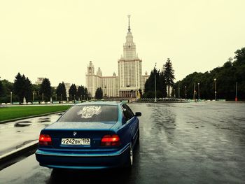 Car on road by buildings in city against sky