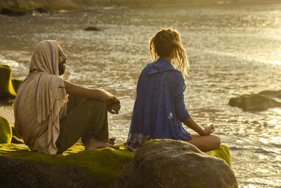 Rear view of people sitting on shore at beach