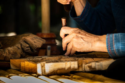 Midsection of man carving wood at table in workshop