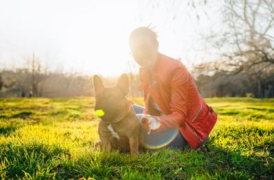 French bulldog and pet owner sitting on grass in the park at sunset