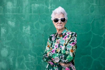 Portrait of woman wearing sunglasses standing against wall