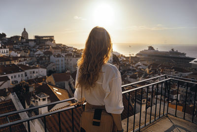 Rear view of woman standing by railing against sky during sunset