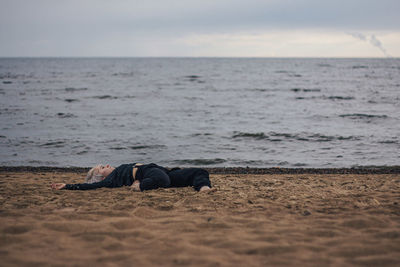 Young woman relaxing on sand at beach against sky