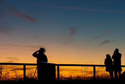 Silhouette people standing against orange sky during sunset