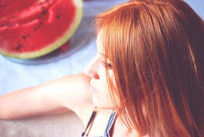  close-up of cropped woman with red hair and watermelon in background