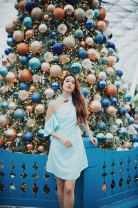 Portrait of smiling young woman standing by christmas tree outdoors