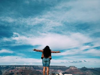 Rear view of woman with arms outstretched standing against sky