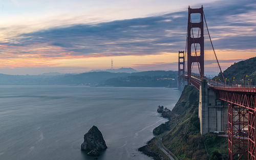 View of suspension bridge over sea against cloudy sky