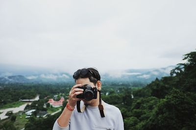 Portrait of woman photographing against sky