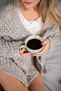 A young woman with a porcelain cup of coffee in her hands.