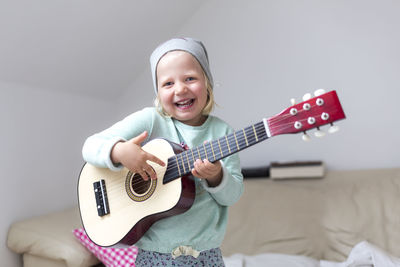 Portrait of happy girl playing guitar at home