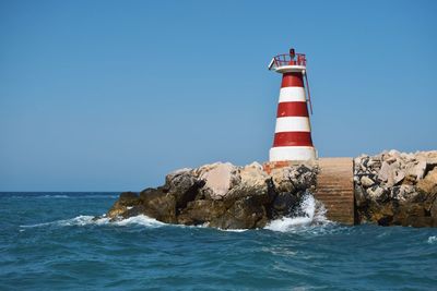 Lighthouse by sea against clear blue sky